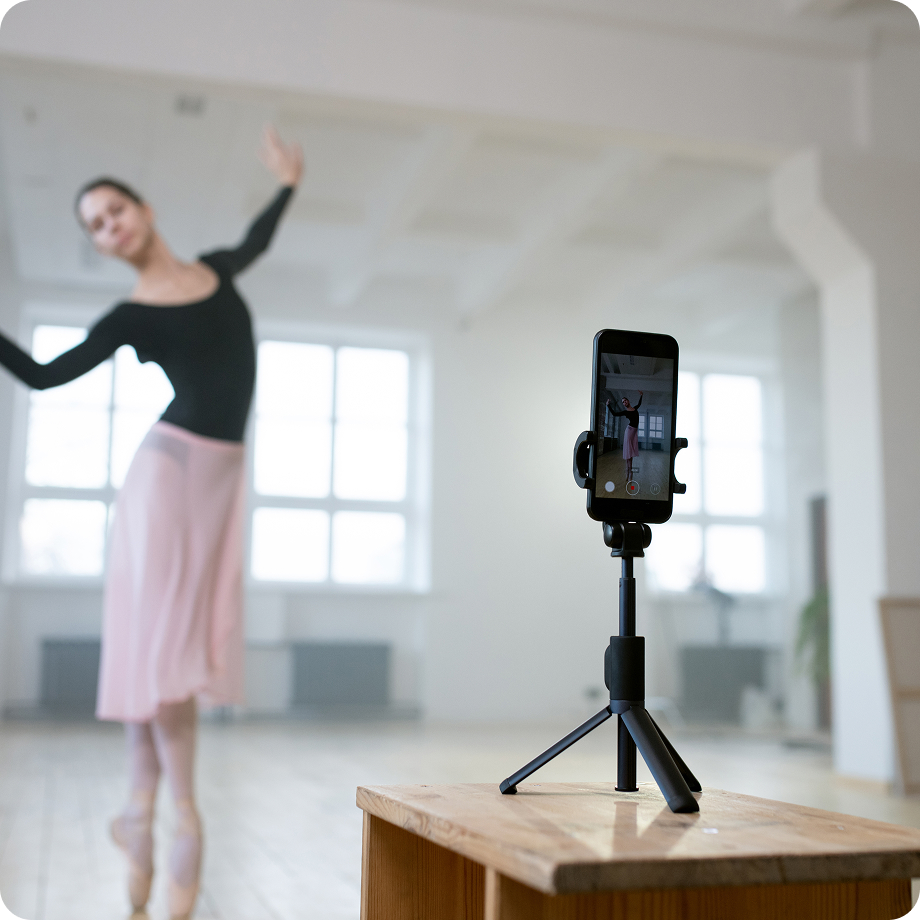 Bailarina con vestido rosa grabándose en un estudio de danza con un smartphone en trípode.