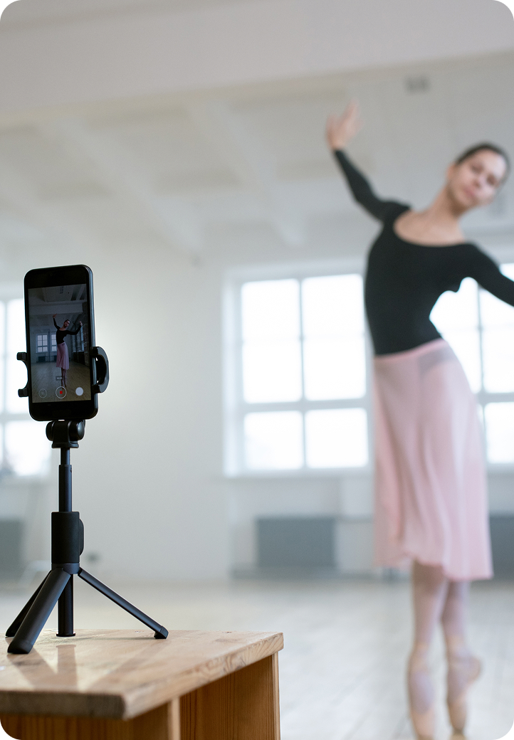 Bailarina de ballet grabando su actuación con un smartphone montado en un trípode, en estudio luminoso.