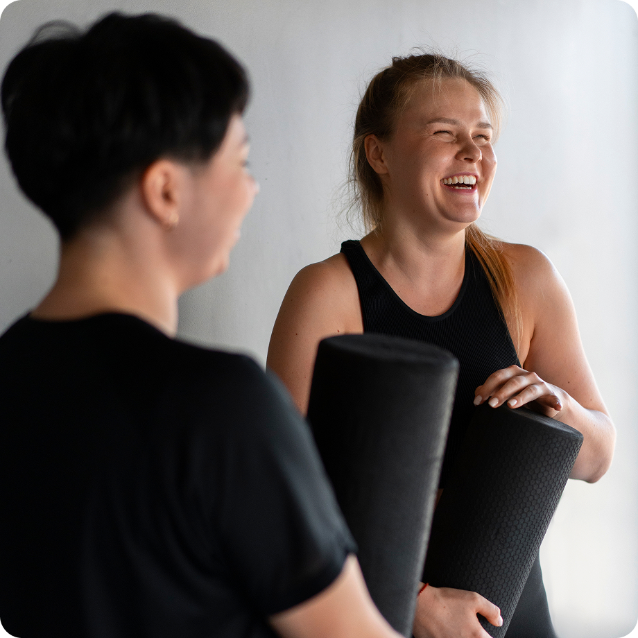 Personas riendo mientras sostienen rodillos de ejercicios negros en un gimnasio, disfrutando de la actividad física.