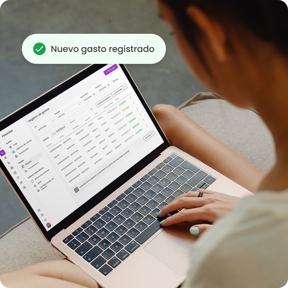 Persona usando portátil para registrar gastos en aplicación de finanzas, icono verde indica nuevo gasto registrado.